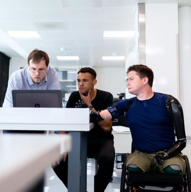 Three people including a person with disability at a desk discussing a work item